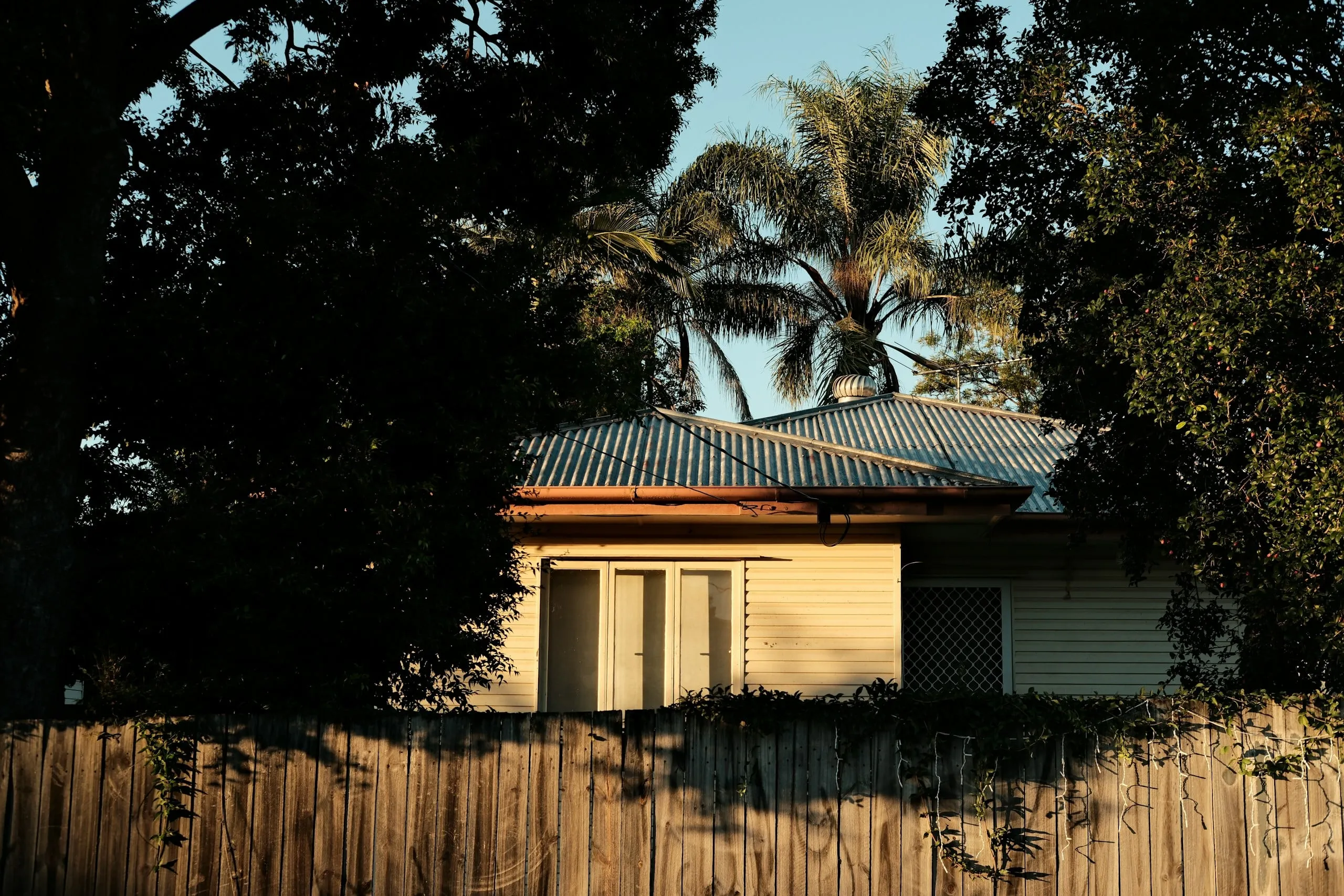 Weatherboard house behind a timber fence in late afternoon light
